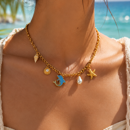 Gold necklace with charms worn by a person against a beach background