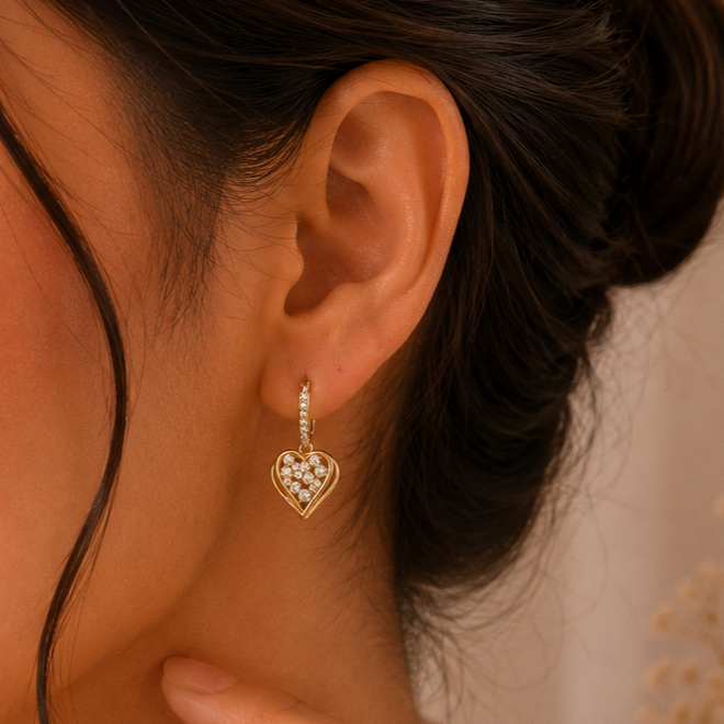 Close-up of a person wearing a gold heart-shaped earring with clear stones.