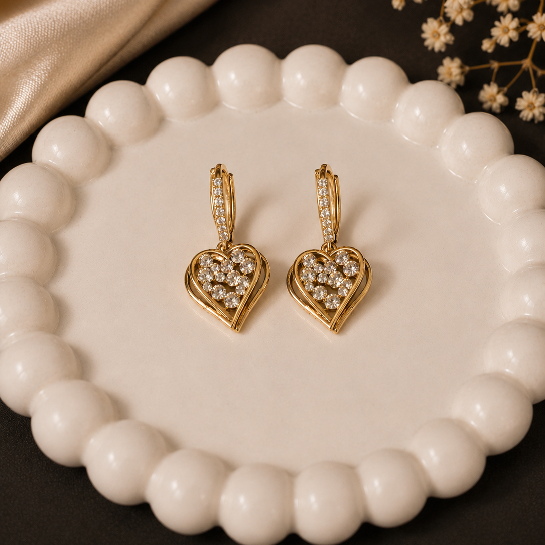 Gold heart-shaped earrings with diamond accents on a white beaded dish.