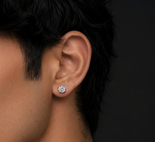 Close-up of an ear wearing a diamond earring with dark hair and skin on a black background