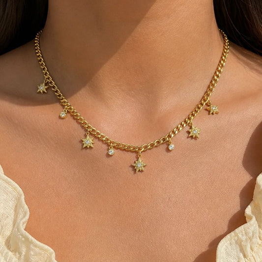 Gold chain necklace with star pendants worn by a person in a light-colored top.