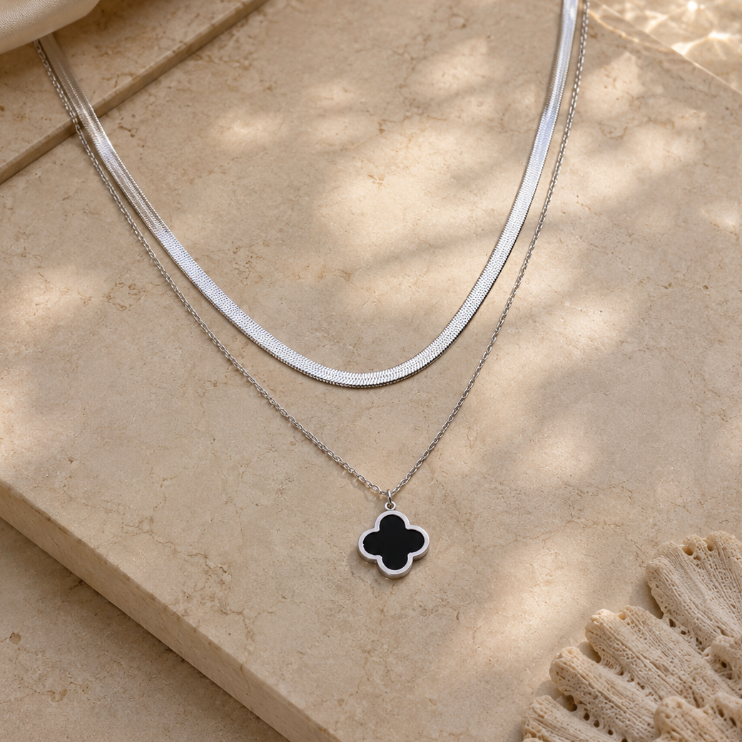 Silver necklace with a black clover pendant on a beige stone surface