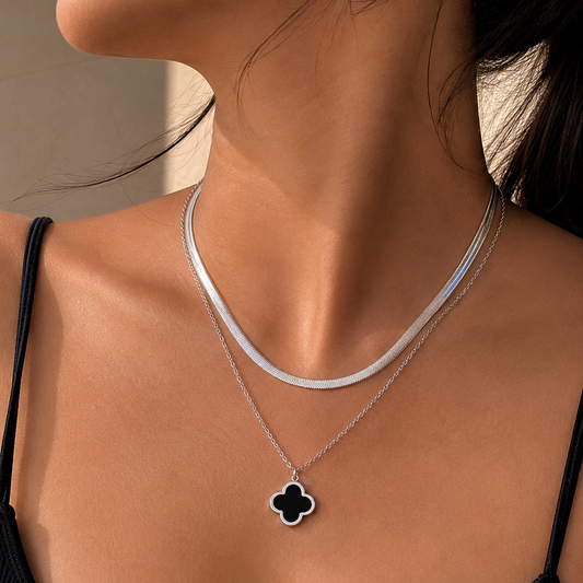 Silver necklace with a clover pendant on a person wearing a black top.