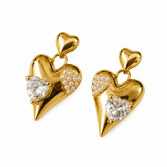 A pair of gold heart-shaped drop earrings with a small heart at the top, a large clear heart-shaped crystal, a smaller clear oval crystal, and a wing-like cluster of tiny white stones on one side, shown on a plain white background.