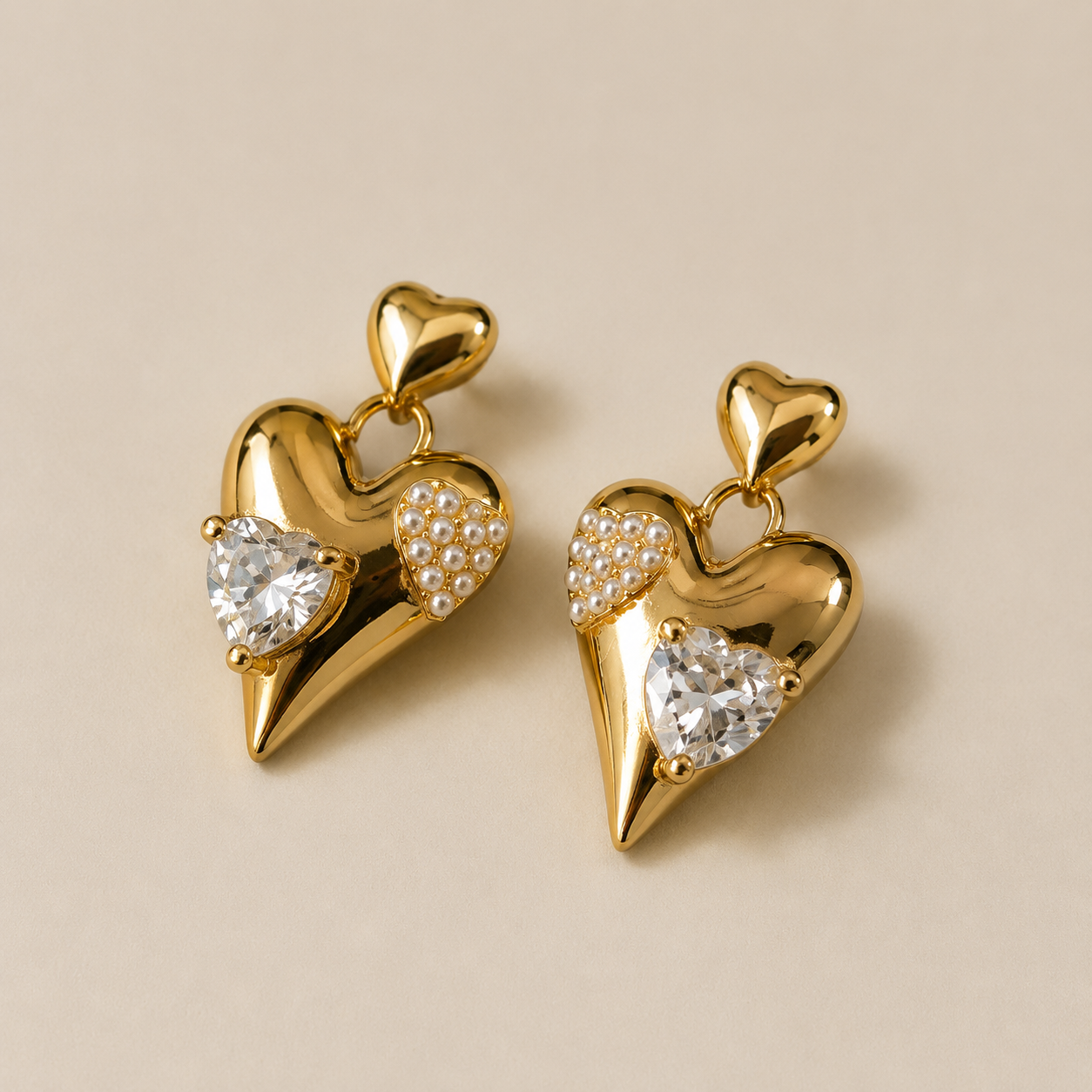Gold heart-shaped earrings with embedded stones on a beige background