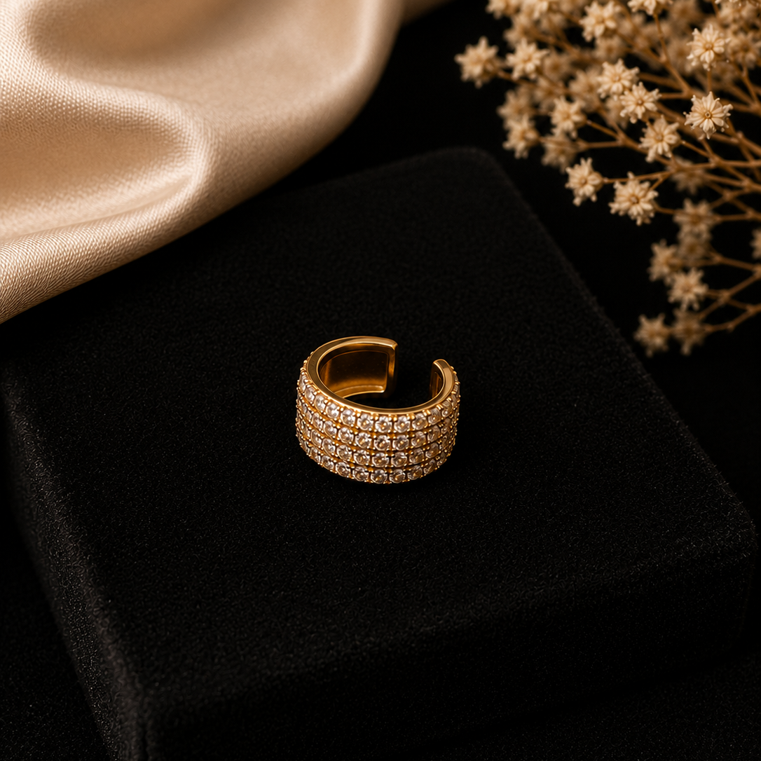 Gold ring with diamond accents on a black surface with beige fabric and dried flowers.