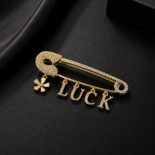 Gold brooch with 'LUCK' and clover charm on a black background