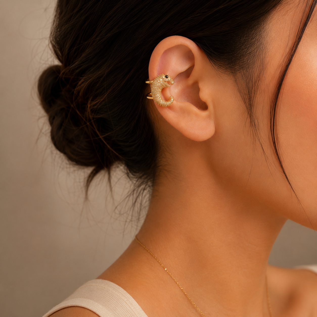 Close-up of a person wearing a gold earring with a textured design against a neutral background