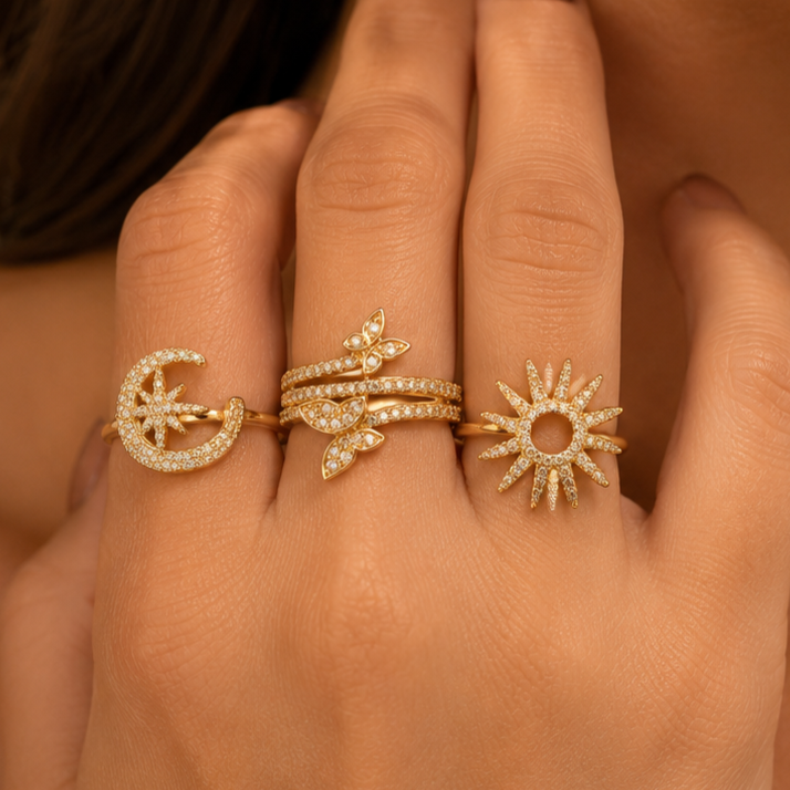Three gold rings with moon, sun, and leaf designs on a hand against a brown background