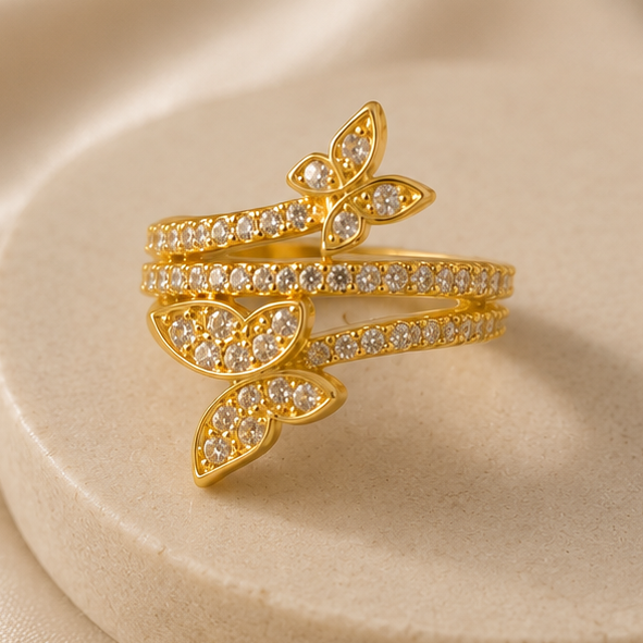 Gold butterfly-shaped ring with gemstones on a beige background
