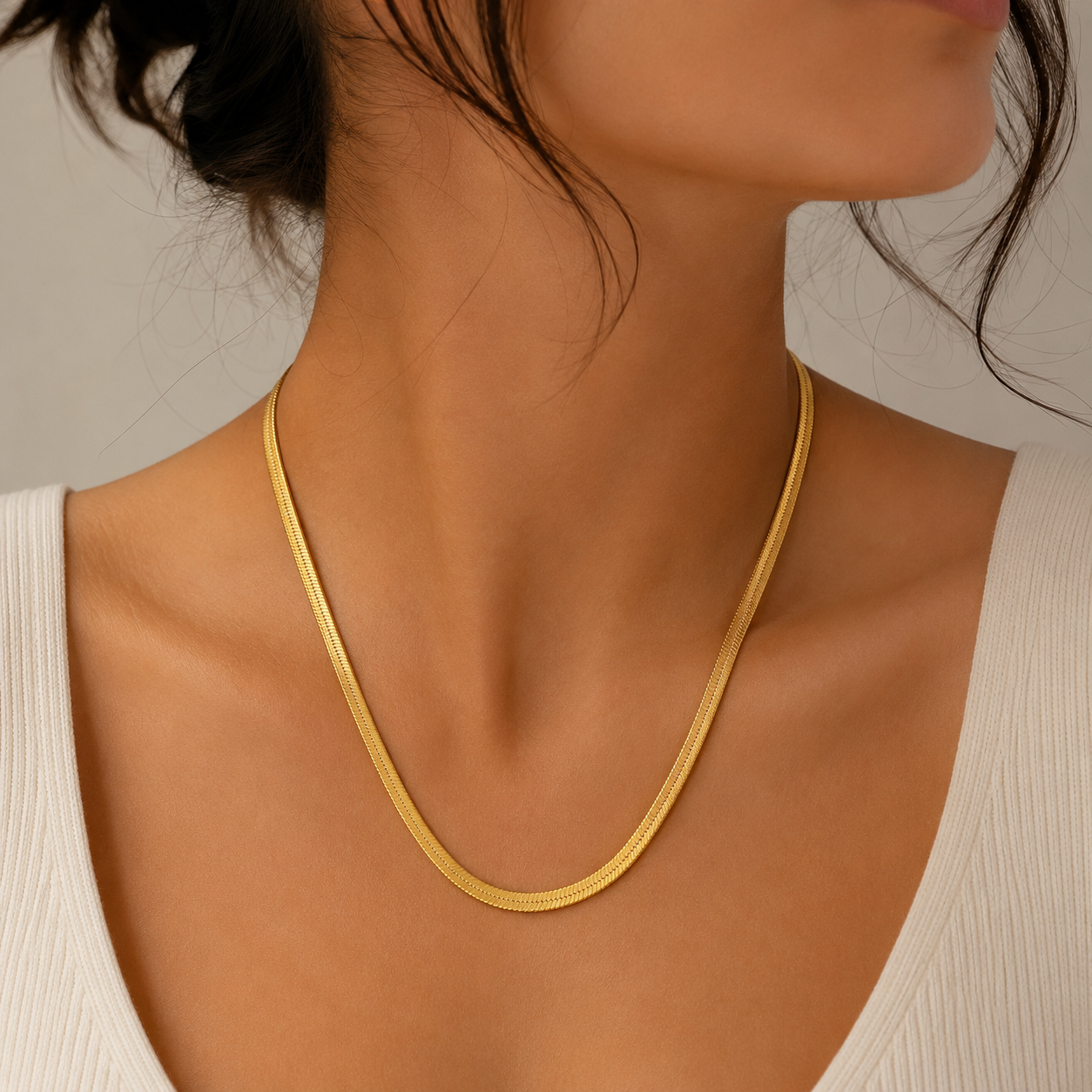 Gold necklace on a person wearing a white top against a neutral background