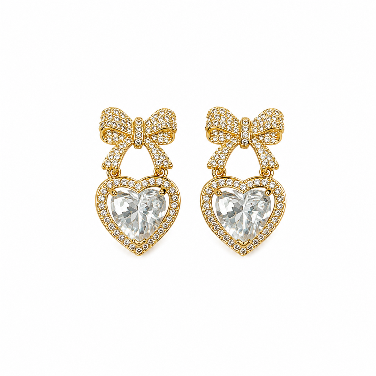 A pair of gold heart-shaped drop earrings featuring a pavé-set clear heart gemstone and a matching pavé bow above it, shown on a plain white background.